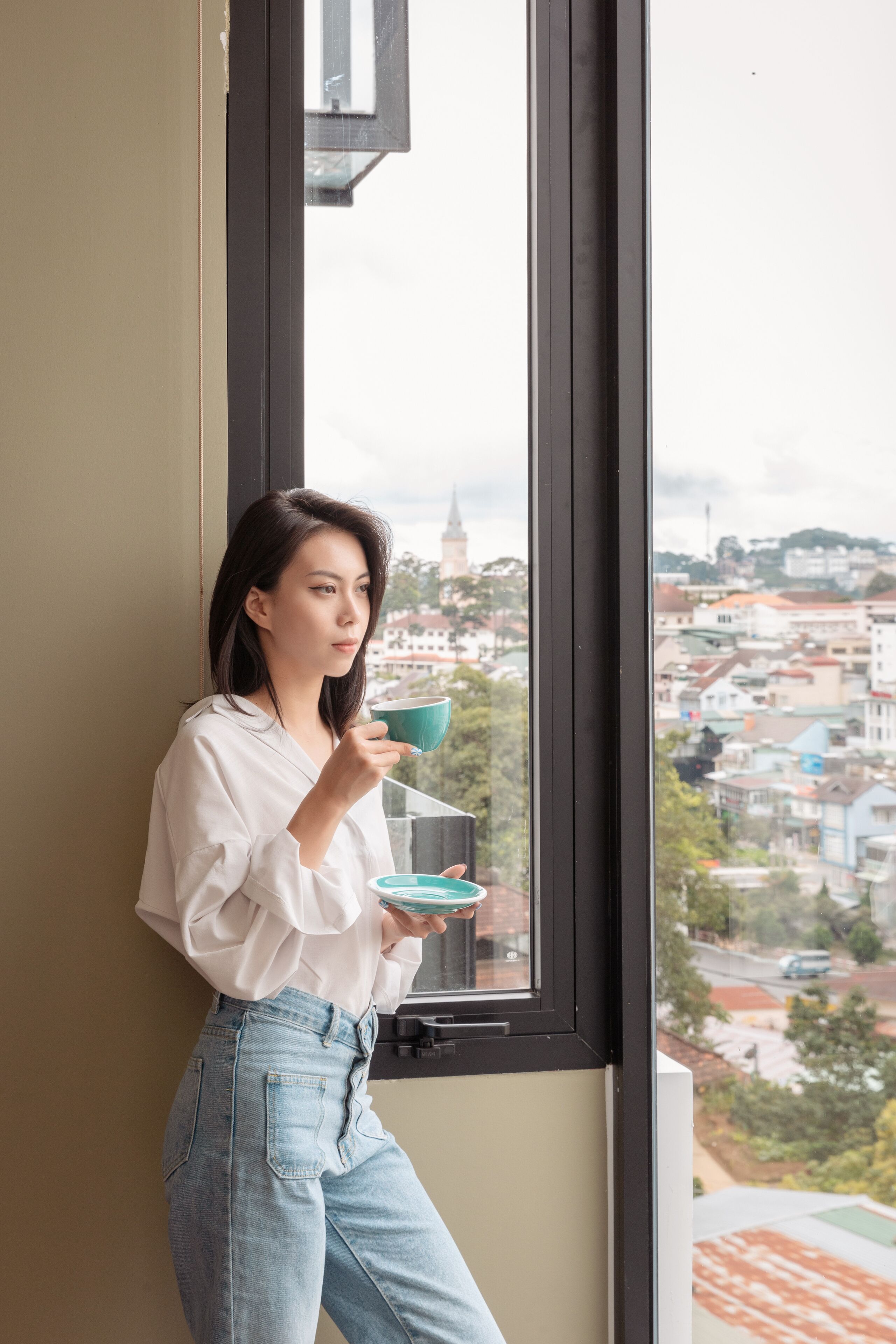 Una persona de pie junto a una ventana con vista a la ciudad.