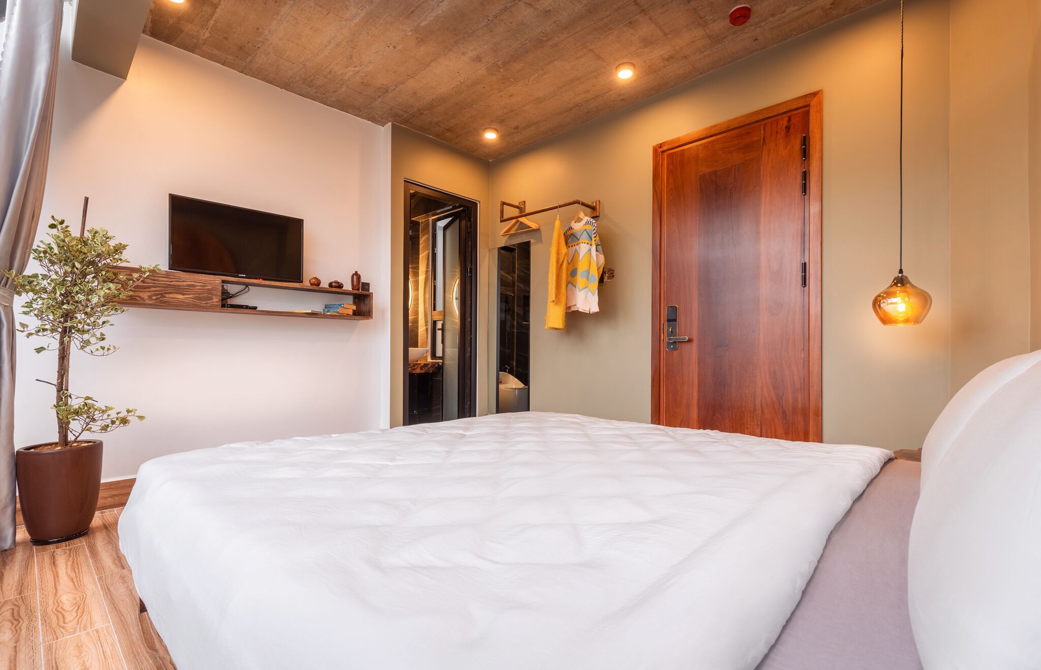 Un dormitorio con una cama, un televisor montado en la pared, una puerta de madera y una lámpara colgante.