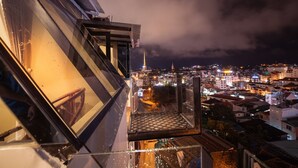 Un edificio alto con vistas a un paisaje urbano nocturno, incluyendo edificios iluminados y una torre destacada.