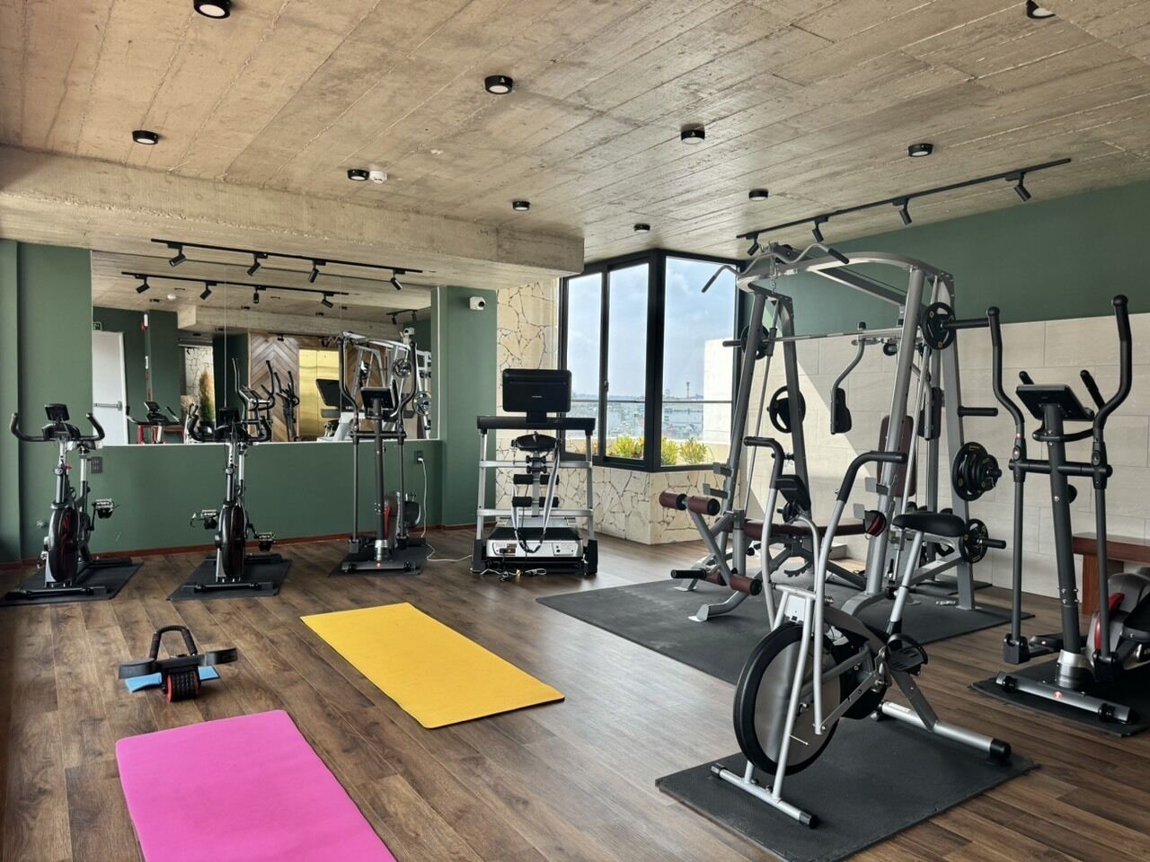 A gym with various exercise equipment, wooden flooring, and large windows.