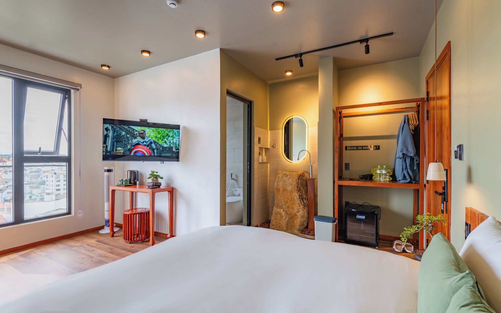 A modern hotel room with a large bed, a television mounted on the wall, a small table with a plant, and a wooden wardrobe.