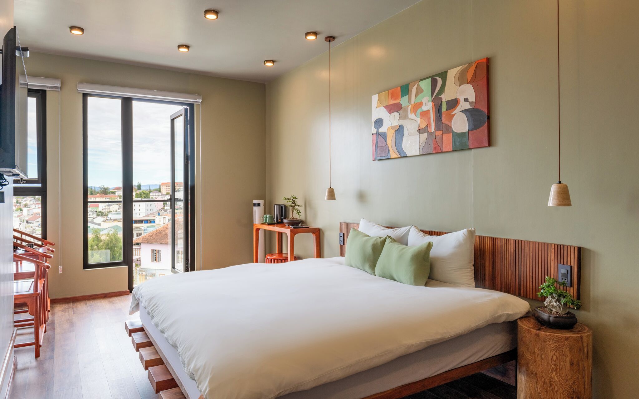 A modern bedroom with a large bed, a view through a sliding door, and a painting on the wall.