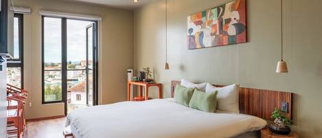 A modern bedroom with a large bed, a view through a sliding door, and a painting on the wall.