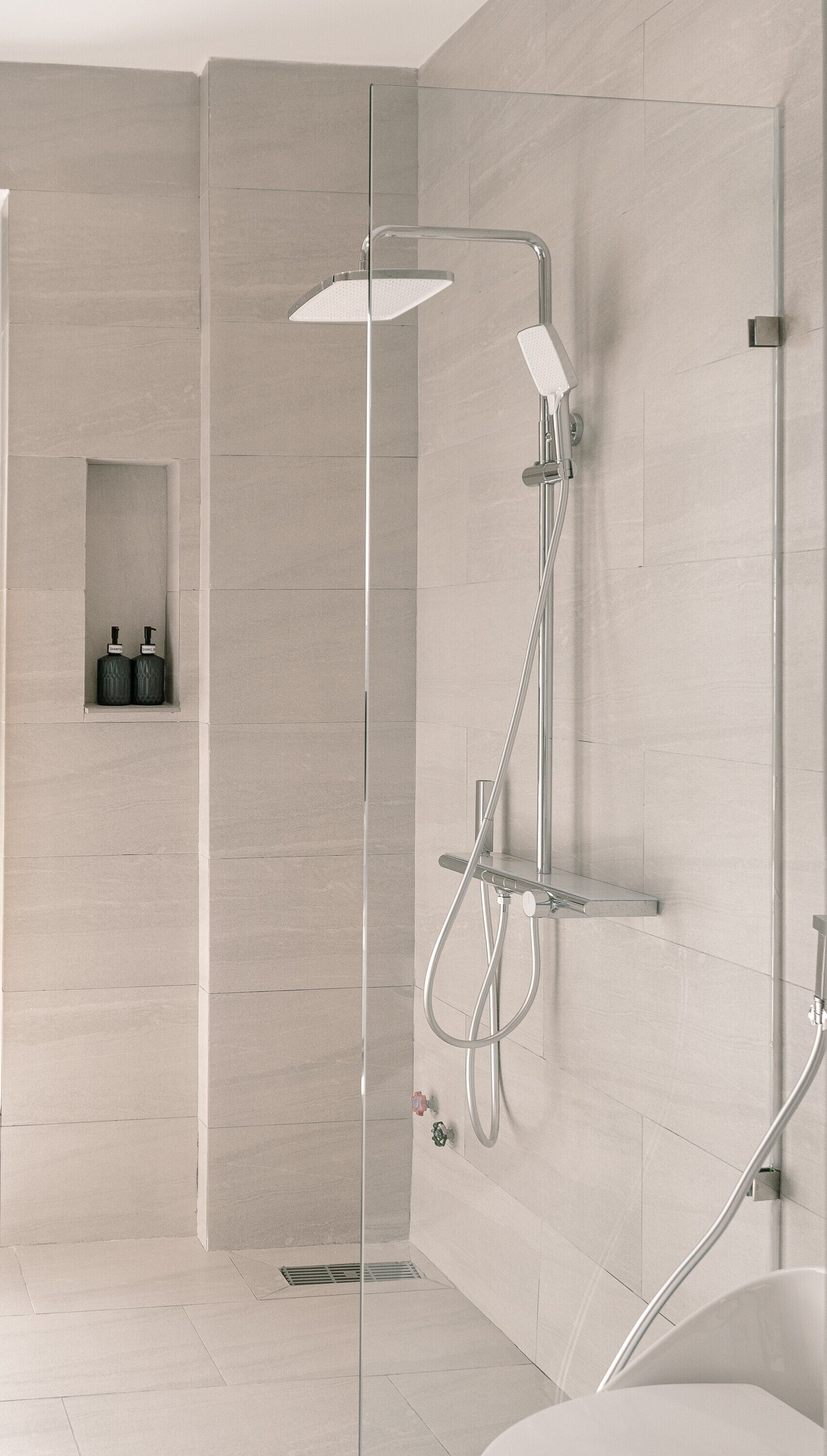 A modern bathroom with a glass-enclosed shower, a handheld showerhead, and a wall-mounted faucet.