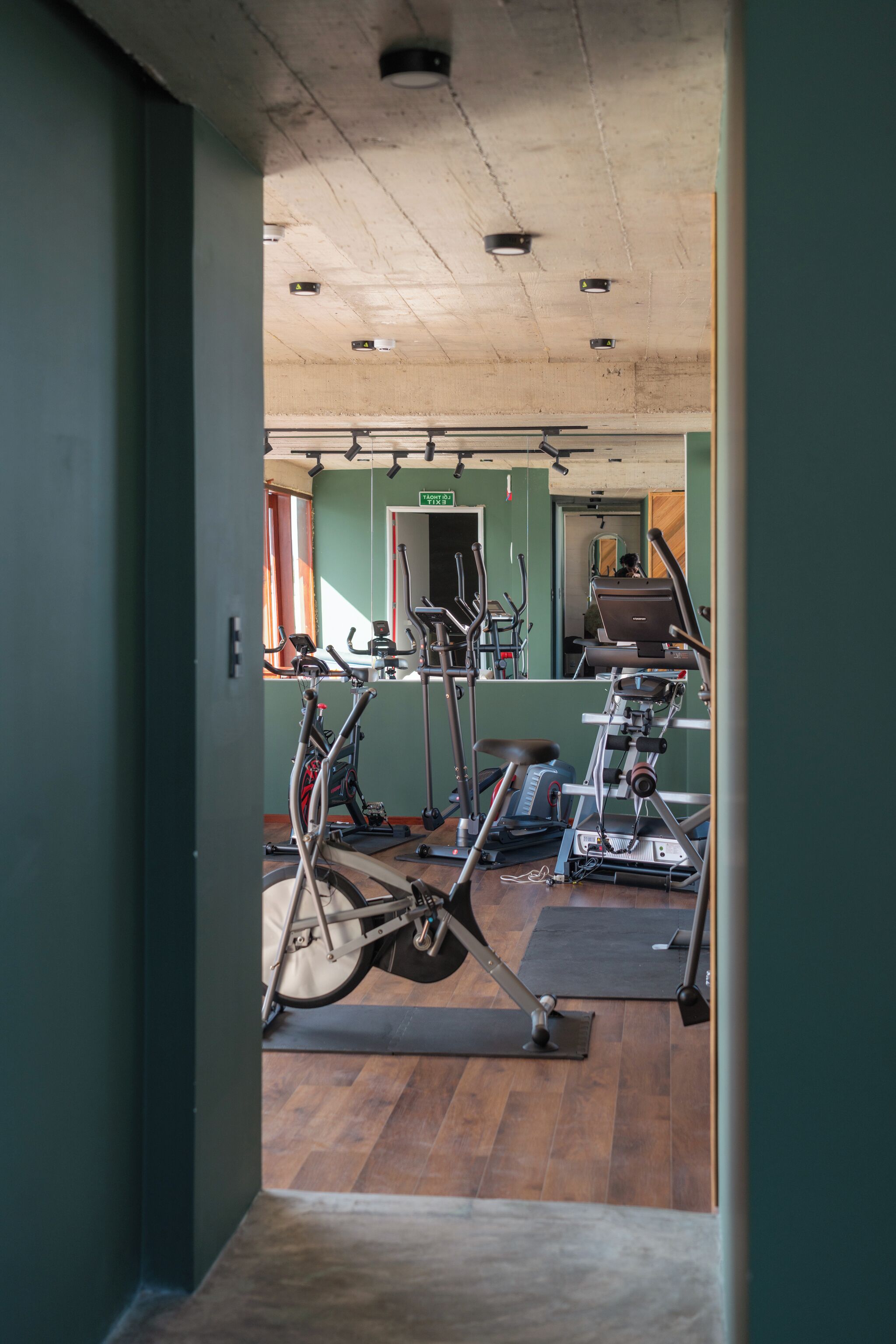 A gym with exercise equipment, wooden flooring, and green walls.
