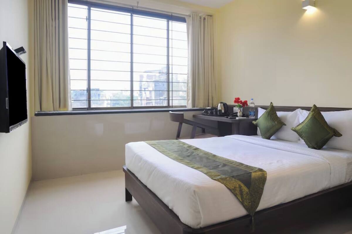 Une chambre d’hôtel avec un lit, un bureau, une chaise et une fenêtre avec des rideaux.