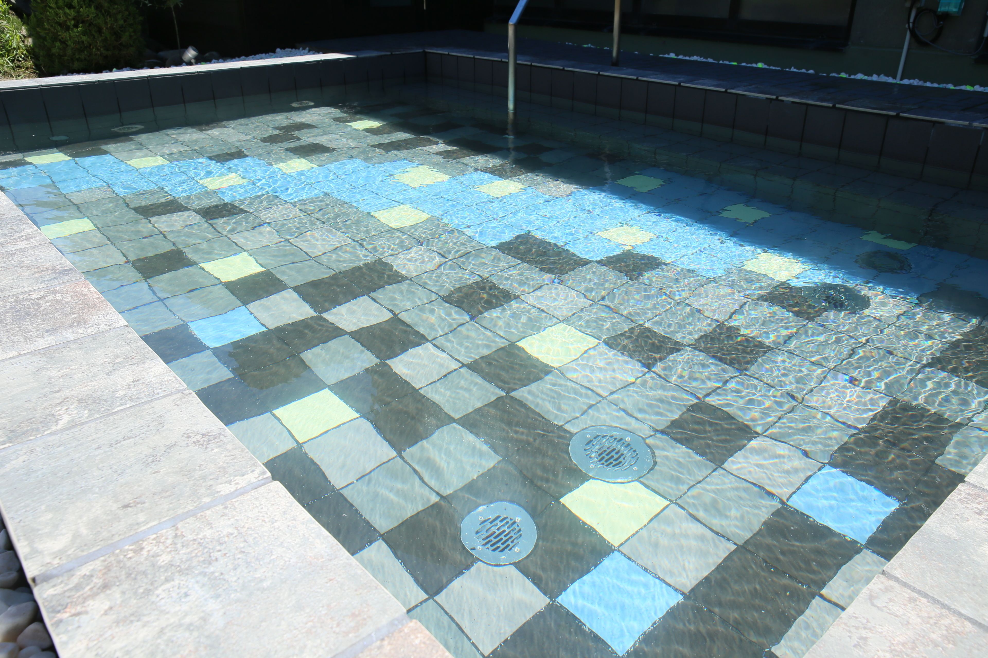 A swimming pool with a checkered tile pattern and two drain covers.