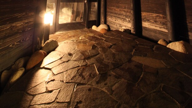 Une pièce aux murs en bois et au plafond en pente, éclairée par une lumière tamisée, et dont le sol est recouvert de pierres.