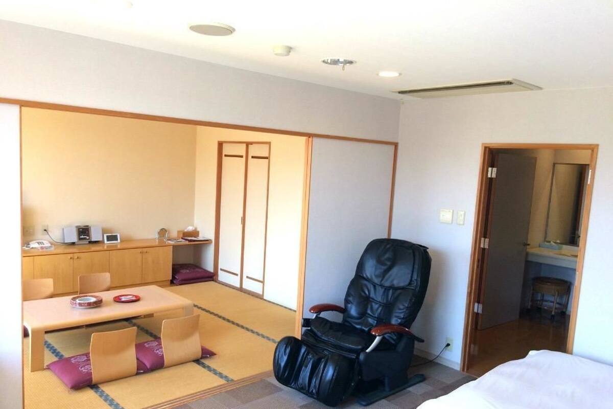 A hotel room with a tatami mat seating area, a massage chair, a bed, and a small kitchenette.