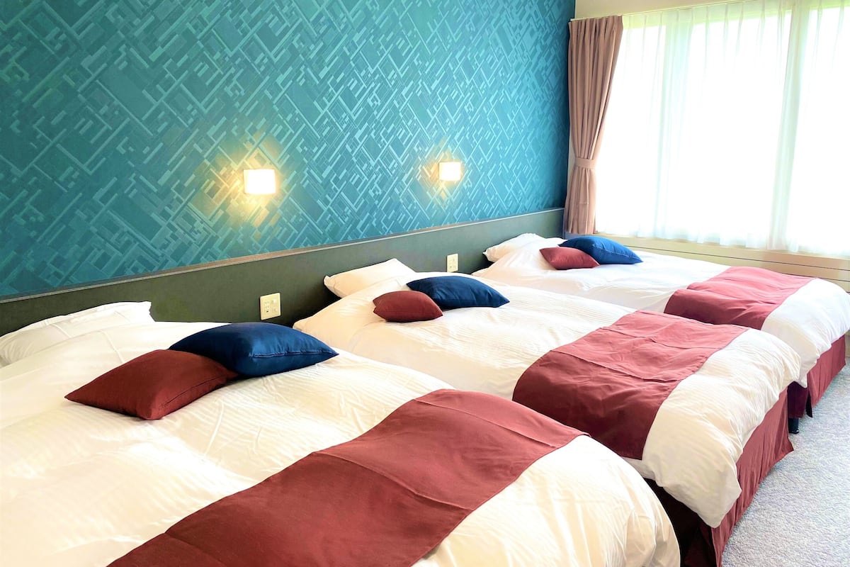 A hotel room with two beds, each with white and red bedding, and a blue patterned wall.