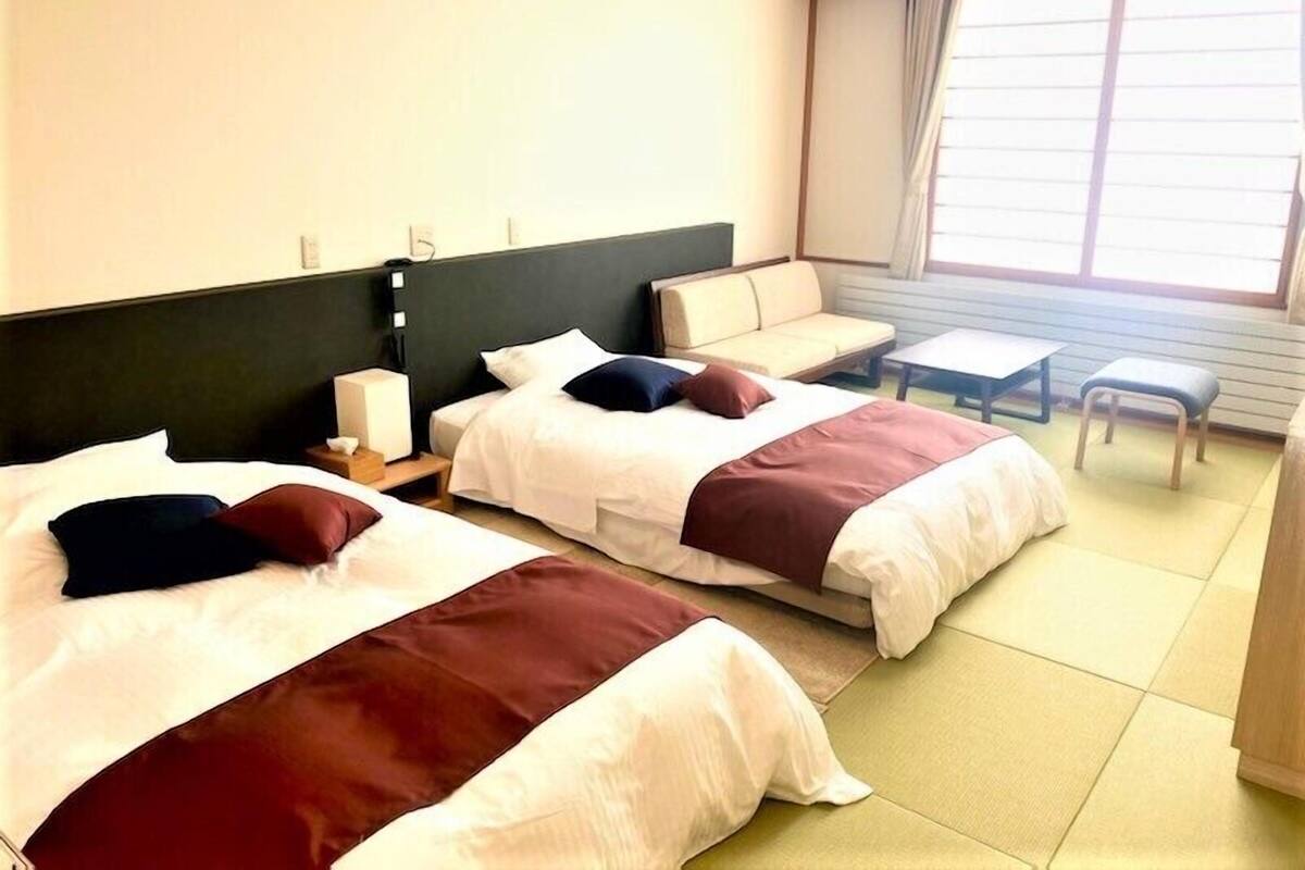 A hotel room with two beds, a sofa, a small table, and a window with curtains.