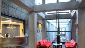 Un hall d’entrée moderne avec un comptoir d’accueil, un espace détente avec des sièges rouges et de grandes fenêtres.