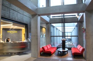 Un vestíbulo moderno con mostrador de recepción, zona de estar con asientos rojos y amplias ventanas.