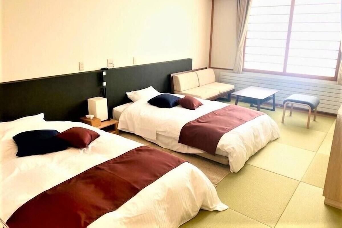 A hotel room with two beds, a sofa, a small table, and a window.