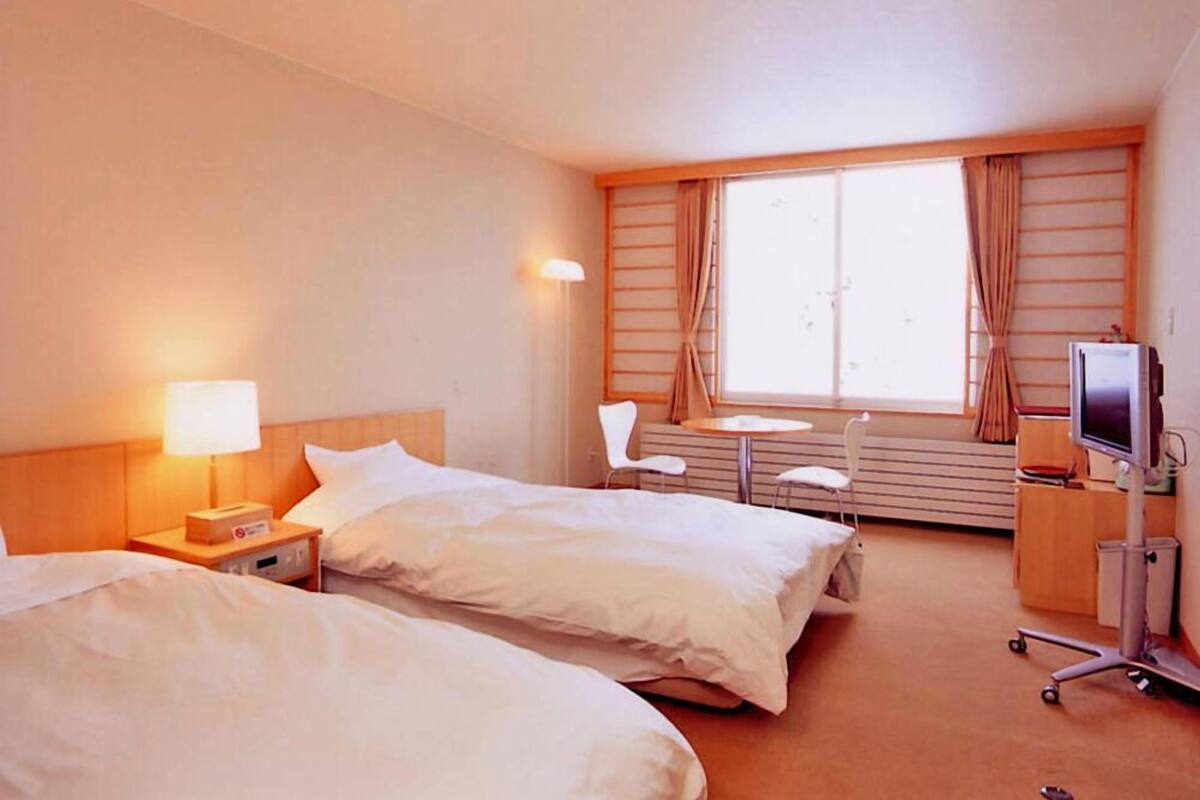 A hotel room with two beds, a desk, a chair, a TV, and a window with curtains.