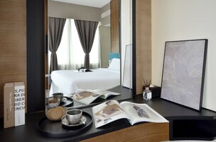 Una habitación de hotel con una cama, una mesita de noche con revistas, una bandeja con galletas y una taza, y un cuadro en la pared.