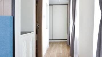 A narrow hallway with a white door at the end, a blue wall on the left, and a grey curtain on the right.