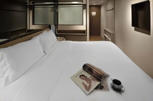 Una cama bien hecha con sábanas blancas, una revista y una taza sobre la mesita de noche.