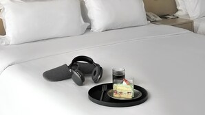 A neatly made bed with white bedding, a pair of headphones, a tray with a dessert, and a bedside phone. - Eco Tree Hotel Causeway Bay (Hong Kong)