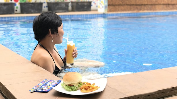 A person relaxing by a pool with a burger and fries on a plate. - Golden Ganesha Villa - Hostel (Siem Reap)