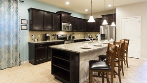 A modern kitchen with dark wooden cabinets, stainless steel appliances, and a granite countertop island with bar stools.
