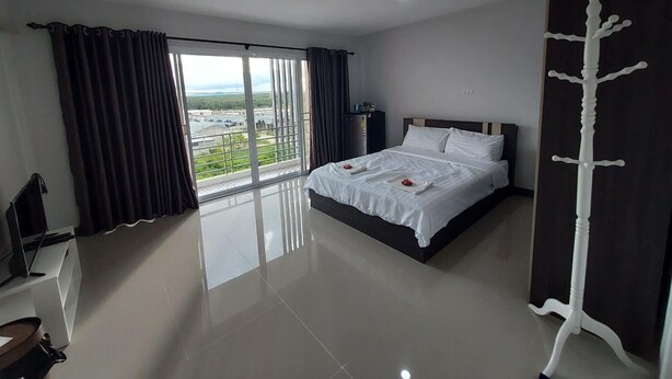 A hotel room with a large bed, a view of the outdoors, a flat-screen TV, and a coat rack. - Thana Apartment (Si Racha)