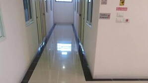 A corridor with a shiny tiled floor, glass doors, and a wall with safety and informational signs. - Thana Apartment (Si Racha)