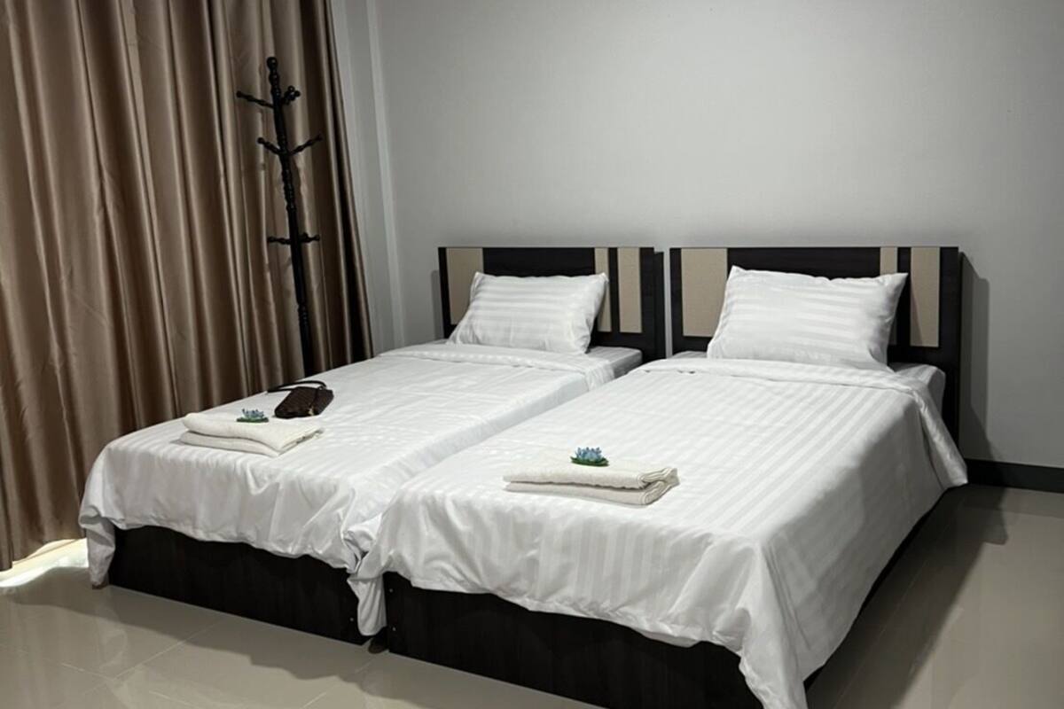 Una habitación de hotel moderna con dos camas, un perchero y un gran ventanal con cortinas.