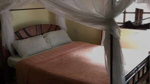 Una cama con mosquitero, cabecera de madera y colcha en tonos claros.