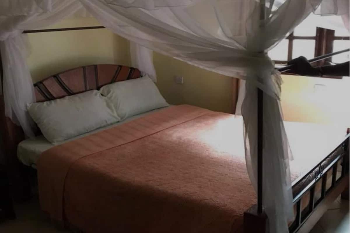 Ein Bett mit Moskitonetz, einem Holz-Kopfbrett und einer hellen Bettdecke.