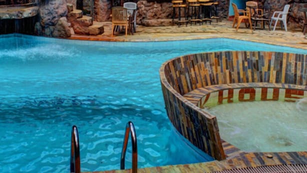 Una piscina con cascada, rodeada de formaciones rocosas y zonas de estar de madera.