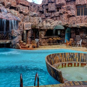 A pool with a waterfall, surrounded by rock formations and wooden seating areas.