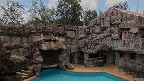Un área de piscina con una pared de roca natural, un jacuzzi y mobiliario exterior.