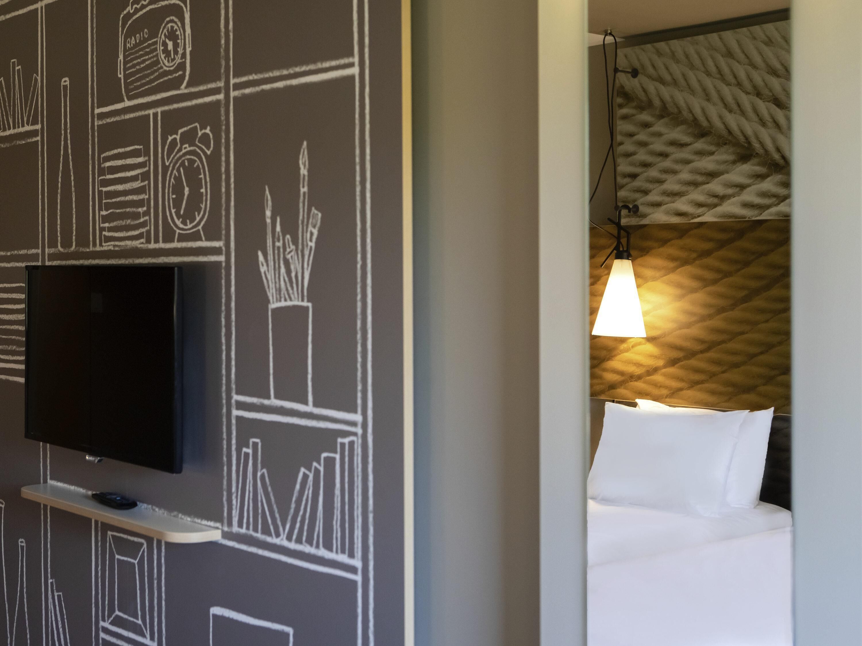 Une chambre d’hôtel dotée d’un téléviseur à écran plat fixé au mur, d’un lit avec du linge de lit blanc et d’un mur à motifs derrière le lit.