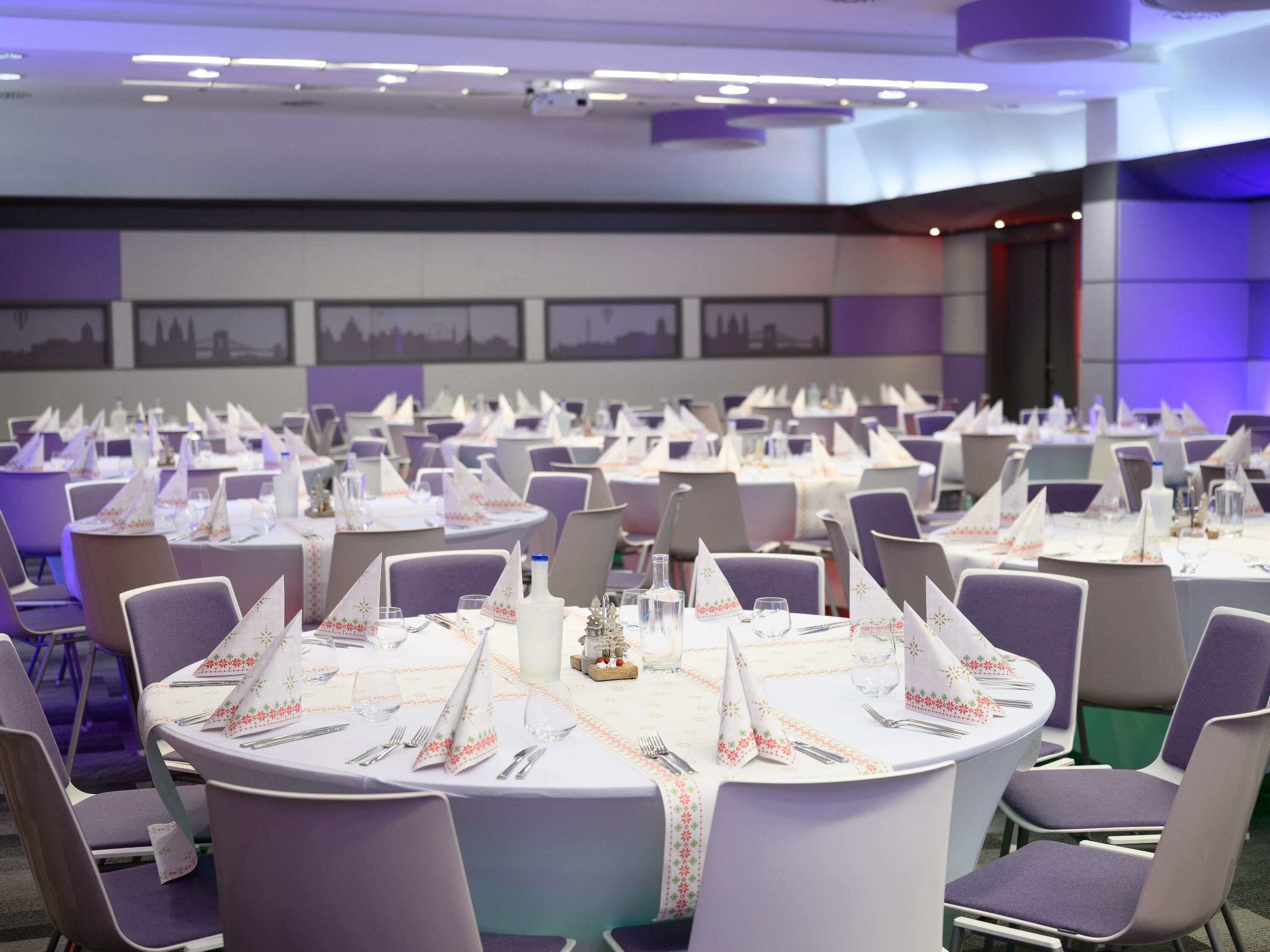 A banquet hall with round tables, purple chairs, and white tablecloths.