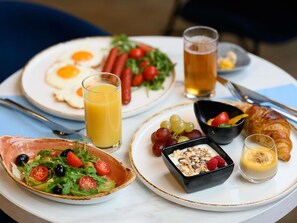 A breakfast setting with plates of eggs, sausages, and a croissant, a bowl of salad, and a glass of orange juice. - ibis Budapest Castle Hill Hotel (Budapest)