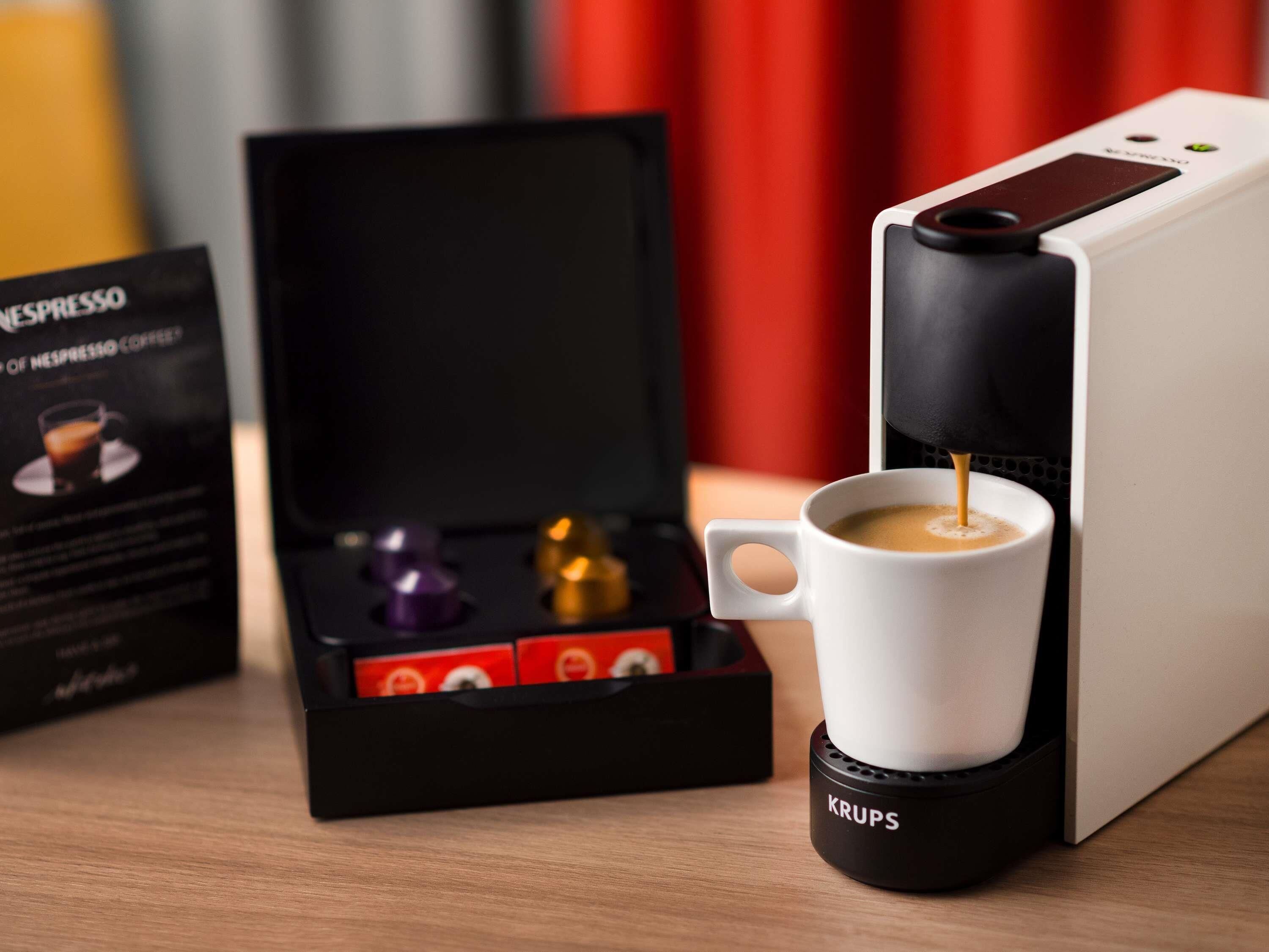 Una cafetera con una taza de café, una caja de cápsulas de café y una cafetera Krups.