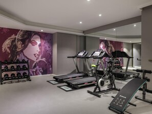 Une salle de sport équipée de tapis de course, d’un banc de développé couché et d’un porte-haltères.