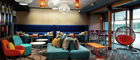 Un área de descanso moderna con un sofá azul, sillas coloridas y un sillón colgante rojo.