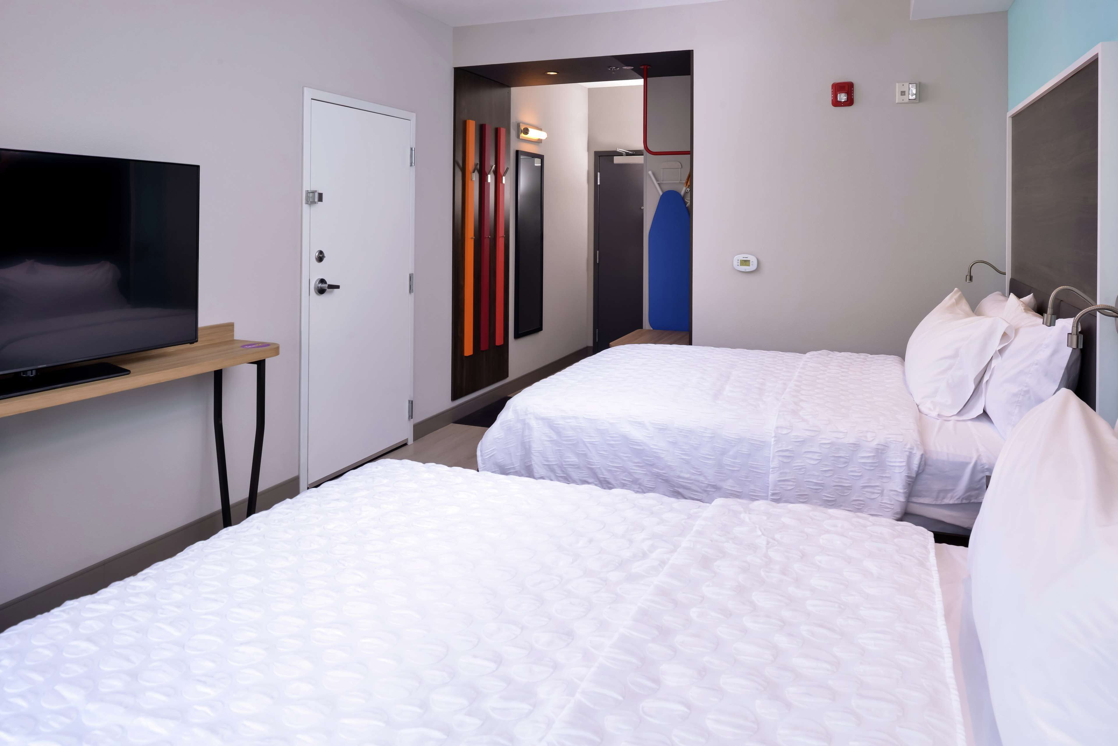 Hotellihuone, jossa on kaksi sänkyä, jalustalla oleva televisio, vaatekaappi ja peili.