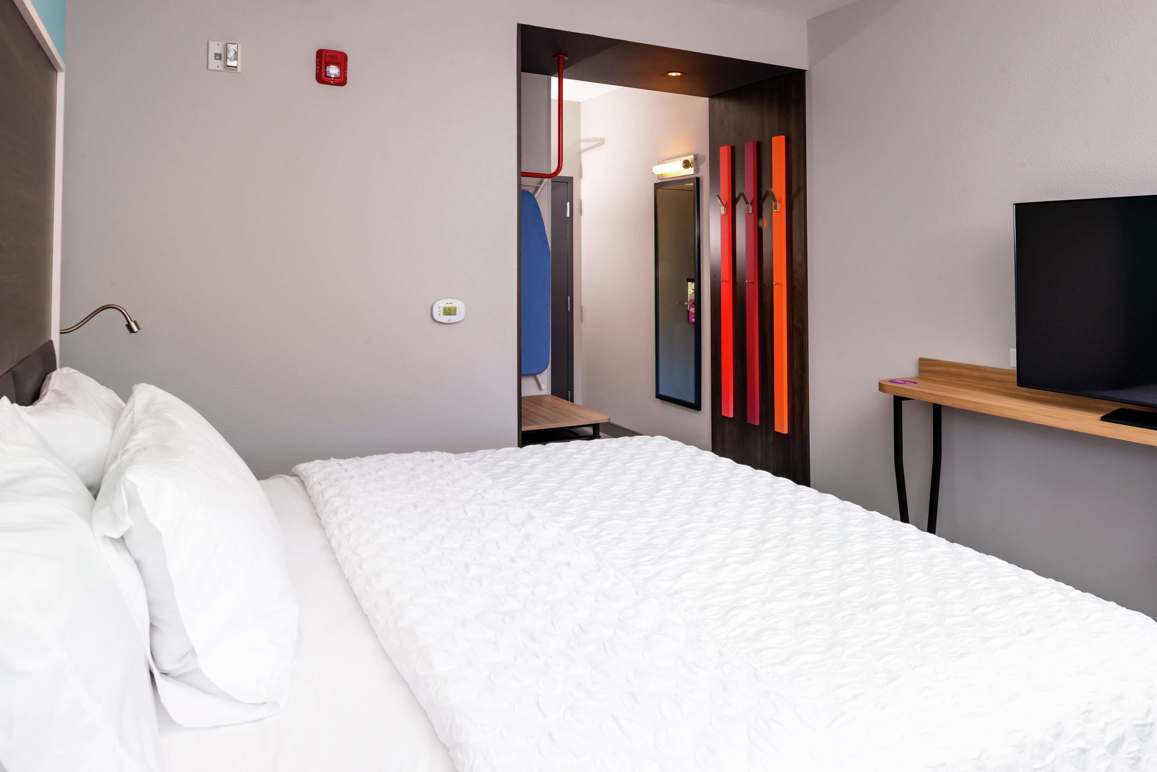 A modern hotel room with a large bed, a TV on a wooden stand, and a mirror on the wall.