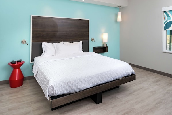 A modern bedroom with a large bed, a red side table, a wall-mounted lamp, and a window with a view.