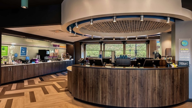 A modern hotel reception area with a curved wooden counter, a digital screen, and a view of the outdoors through large windows. - Tru By Hilton Staunton (Staunton)