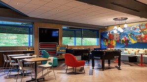 A modern indoor space with tables, chairs, a foosball table, and a mural on the wall. - Tru By Hilton Staunton (Staunton)