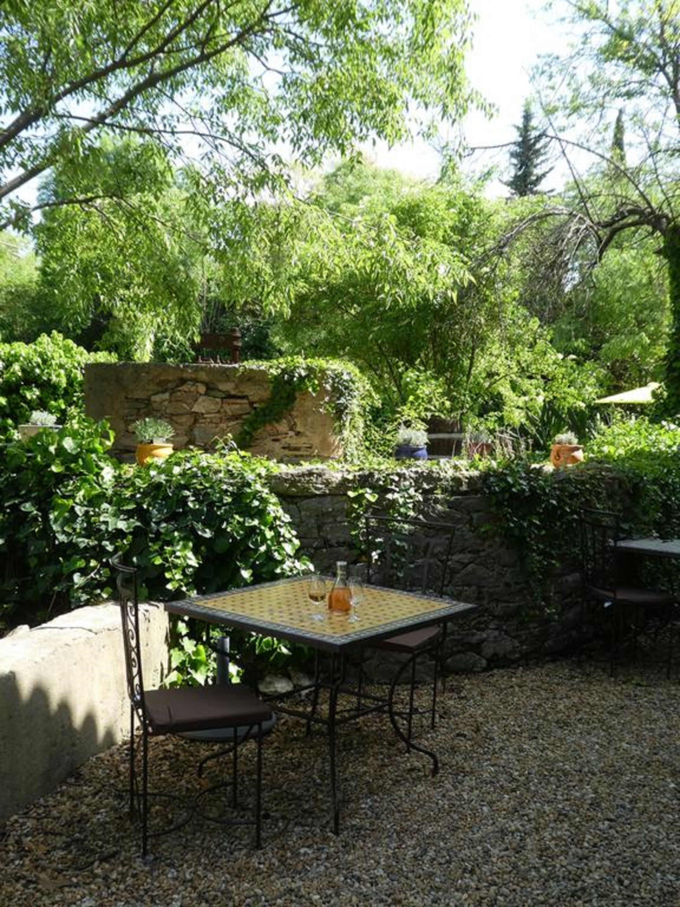 Eine Terrasse im Freien mit Tisch und Stühlen, umgeben von Grünpflanzen und einer Steinmauer.