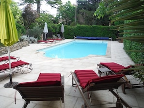 A swimming pool with red lounge chairs and umbrellas, surrounded by greenery. - Eloi Merle B&B (Olonzac)