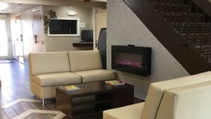Ein Wohnzimmer mit einer Couch, einem Couchtisch und einem Kamin. An der Wand ist ein Fernseher angebracht, und eine Tür ist mit "Business Center" beschriftet.