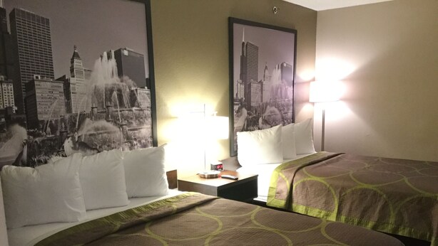 Ein Hotelzimmer mit zwei Betten, einem Nachttisch, einer Lampe und einem Stadtblick-Poster an der Wand.