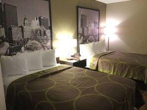 Une chambre d’hôtel avec deux lits, une table de chevet, une lampe et une affiche représentant un paysage urbain accrochée au mur.