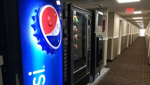 Ein Flur mit Getränkeautomaten, darunter ein Pepsi-Kühler, und einem Hinweisschild für den Ausgang.